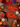 Two red fabric pet collars with a Day of the Dead skeleton print are displayed on a rustic wooden table surrounded by Halloween decorations, including sugar skulls, papel picado, marigolds, and candles. One collar is styled with a black ribbon bow, and both have a circular white sticker reading 'Louis Phil'.