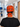 A person viewed from behind wearing a bright orange surgical scrub cap with a black ribbon tie, featuring a Halloween cat print and the text 'I FOUND THIS HUMERUS'. The background shows a blurred hospital hallway.