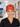 A smiling woman in a hospital or clinic hallway wearing a bright orange surgical scrub cap with cartoon characters and the text 'I FOUND THIS HUMERICUS', paired with black scrubs.