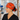 A woman in a hospital hallway wearing a bright orange Halloween-themed scrub cap with cartoon skeletons and the text 'I FOUND THIS MEMORABLE', paired with black scrubs.