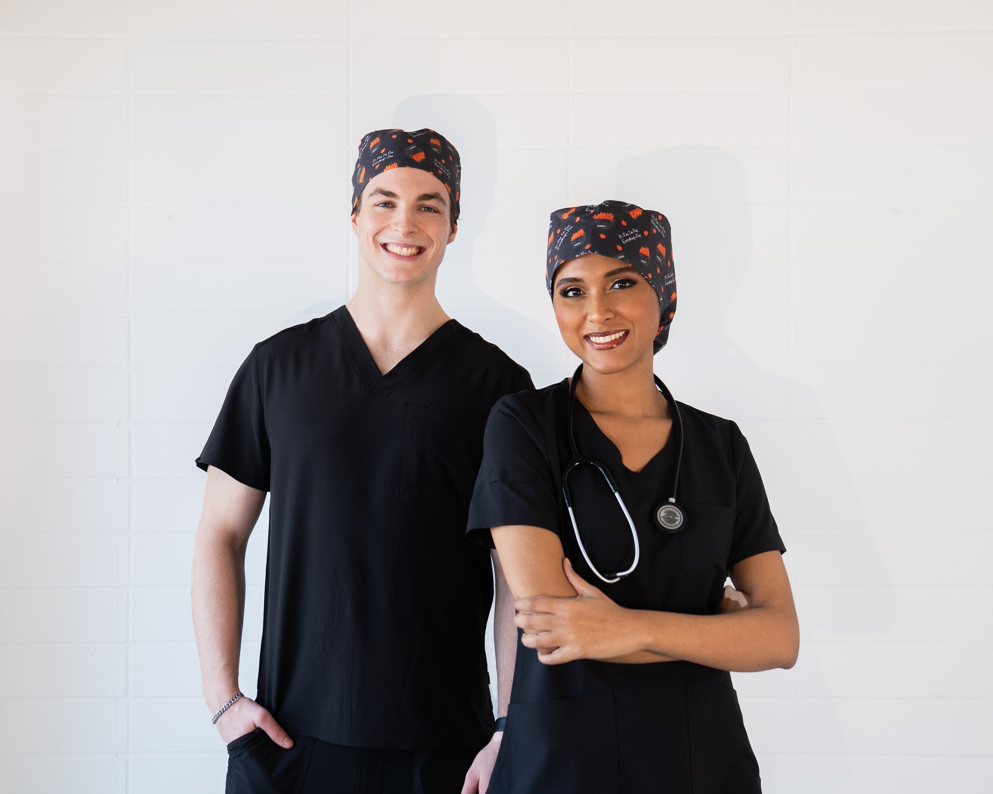 A man and woman in the medical field wearing black scrubs and Louis and Phil scrub caps.